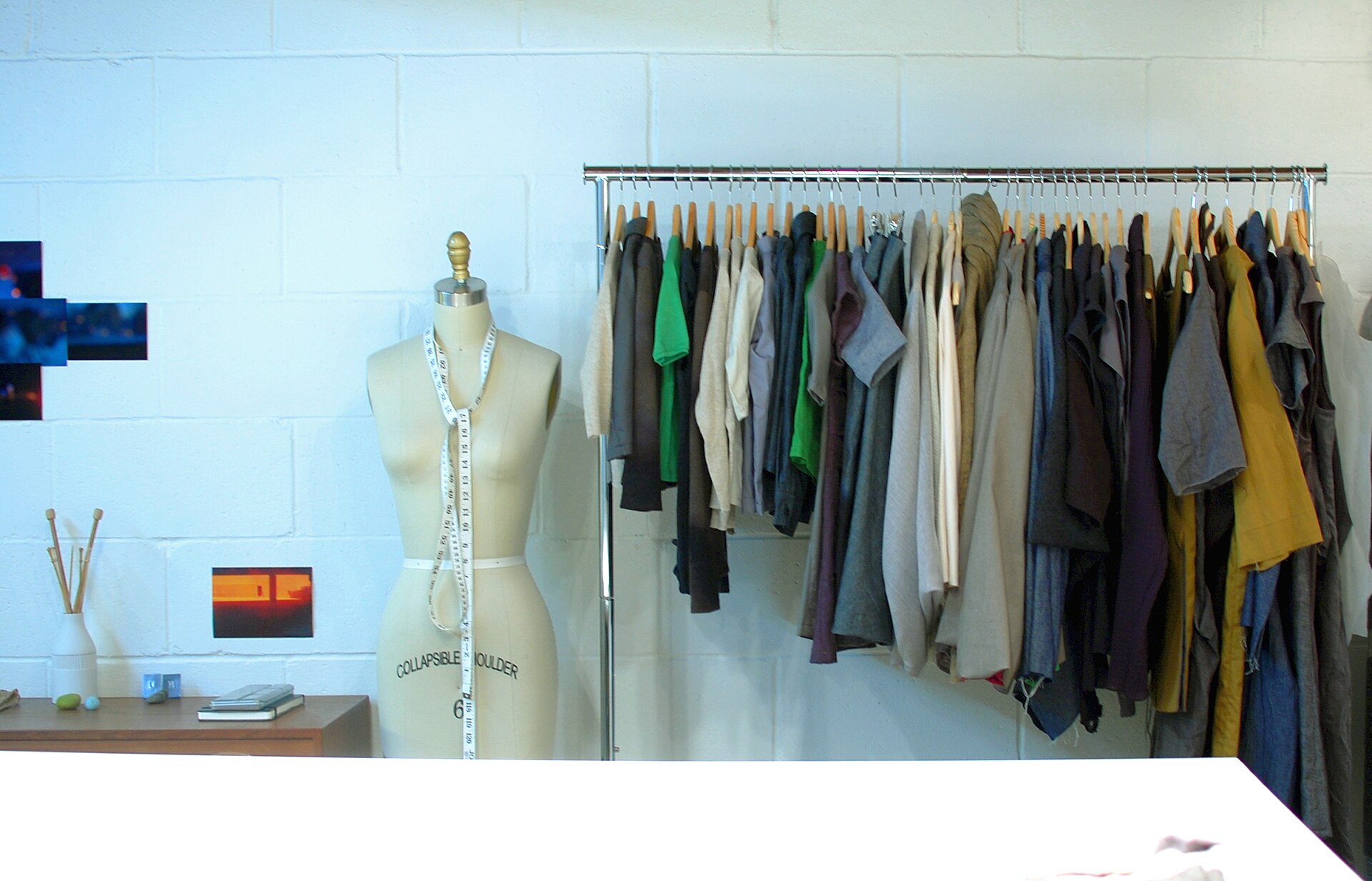 A tailor's dress form beside a rail of garments in mixed colours in a white studio