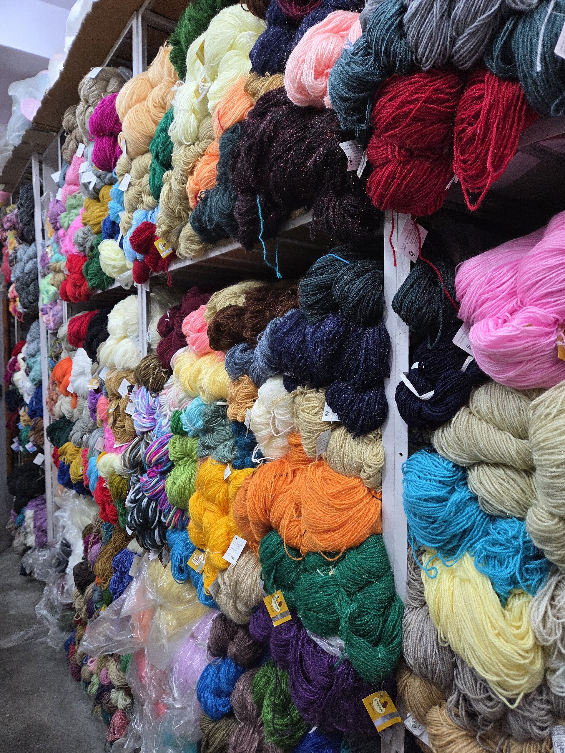 A variety of colorful yarn skeins displayed in a shop, used for knitting, crocheting, and other textile crafts.